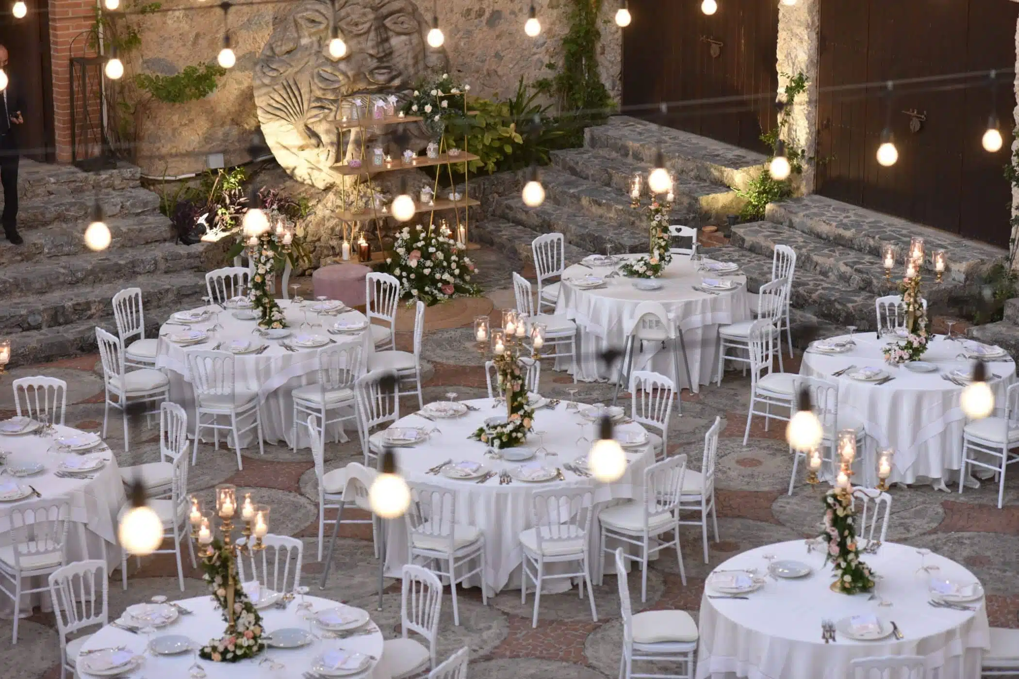 Tavoli allestiti per matrimonio all'aperto con decorazioni floreali eleganti, luci soffuse e atmosfera romantica, perfetta per wedding planner e eventi nuziali di classe.