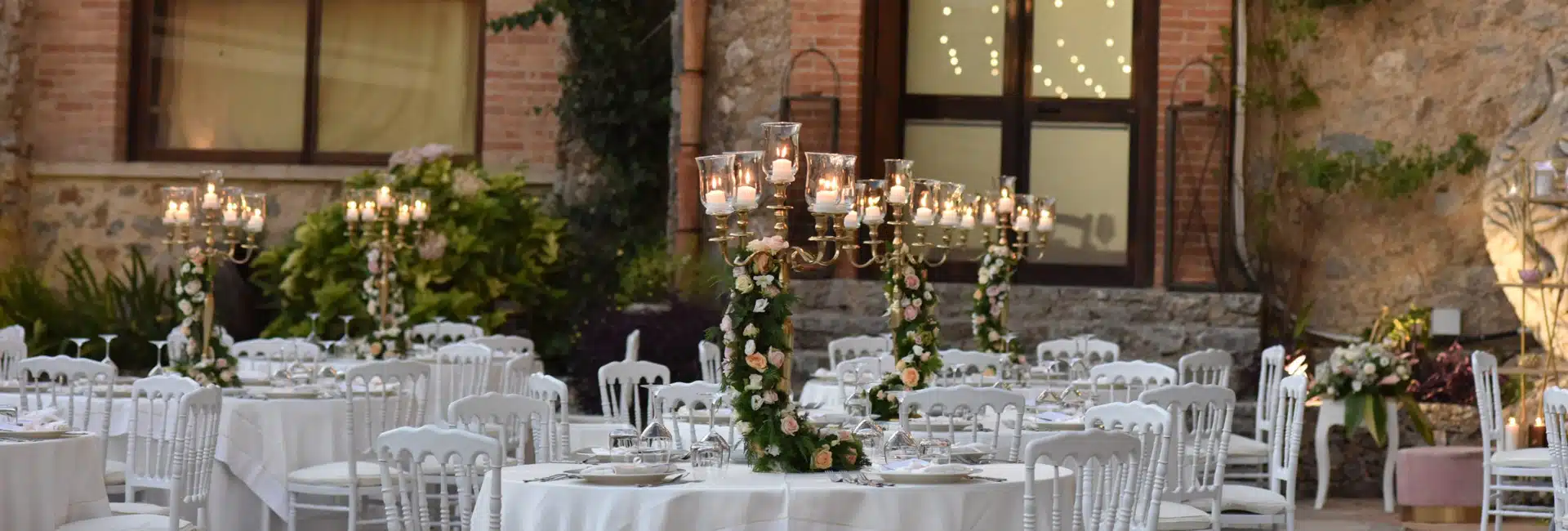 Elegante scena di ricevimento nuziale all'aperto con candelabri decorati con fiori, tavoli imbanditi e atmosfera romantica, ideale per wedding planner chiara B events.