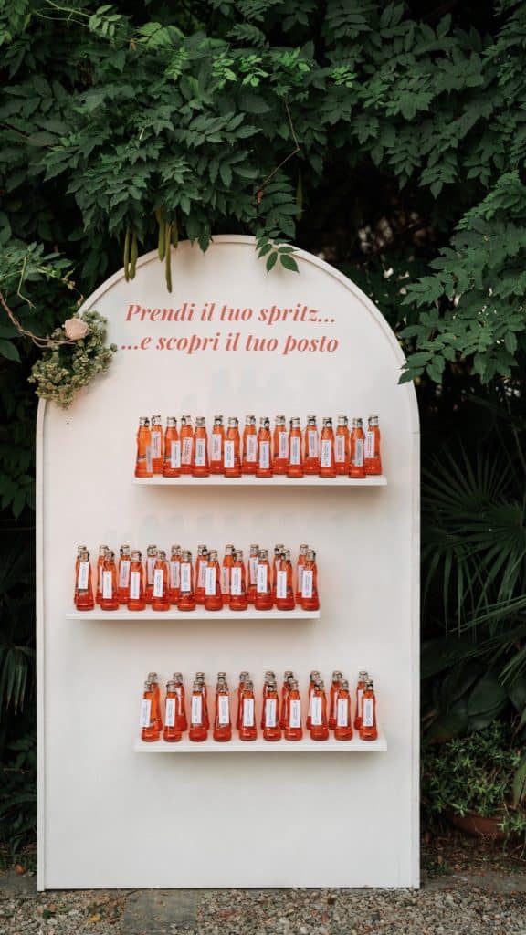 Bottiglie di spritz personalizzate per un matrimonio o evento speciale, ideali come omaggi per gli ospiti, organizzate su scaffali in un allestimento elegante e naturale, perfette per un wedding planner di Chiara B Events.