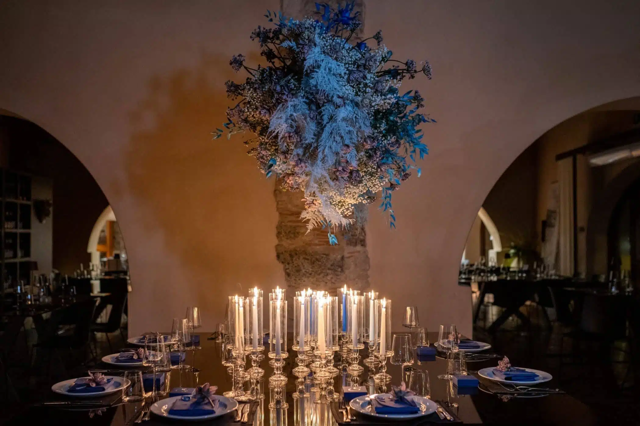 Elegante chandelier di fiori bianchi e blu, decorato con candele accese su tavola da matrimonio presso ChiaraB Events Wedding Planner, creando un'atmosfera romantica e sofisticata per matrimoni esclusivi.