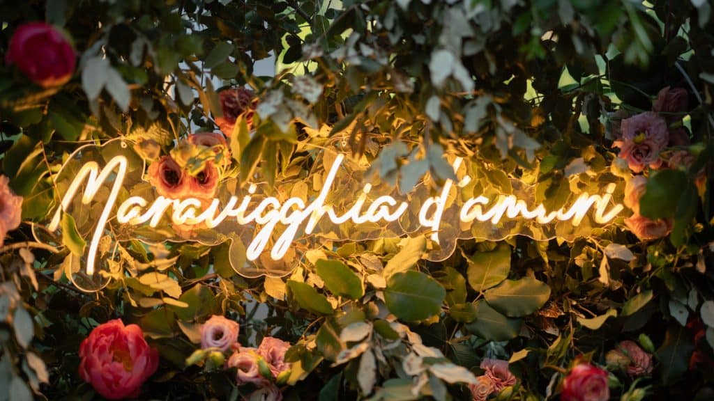 Pianta di fiori e foglie con insegna luminosa in stile neon "Paravighia d'amuri" per eventi e matrimoni.
