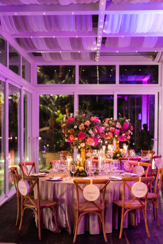 Fondo elegante di un evento di matrimonio con decorazioni floreali di lusso e illuminazione soffusa in una sala con ampie vetrate, pensato per matrimoni chic e wedding planner professionisti.
