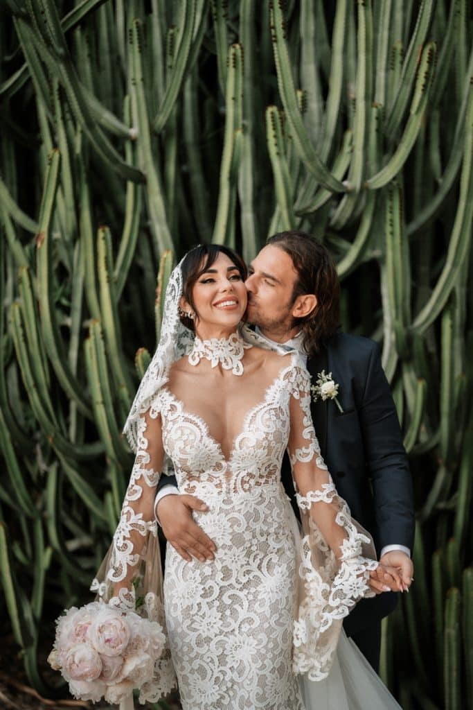 Sposa con abito in pizzo floreale, sposo in abito blu scuro, coppia felice in matrimonio, dettaglio di wedding planner ChiaraB Events, decorazioni nuziali eleganti, servizio wedding planning, fotografie matrimonio romantico, organizzazione eventi matrimonio Italia.