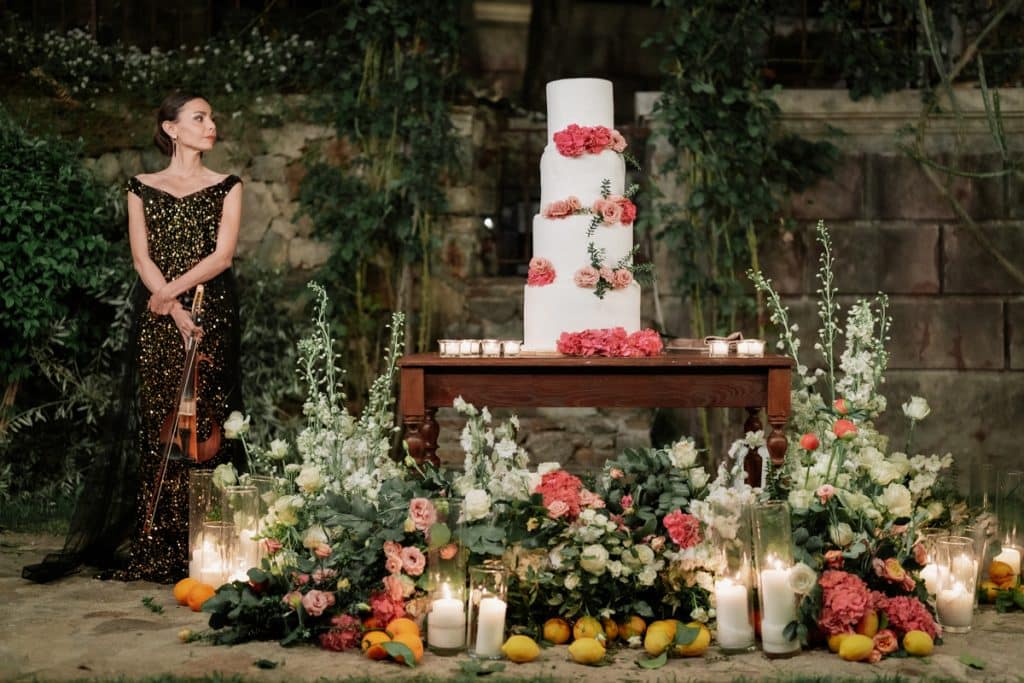 Nei, questa immagine rappresenta una cerimonia di matrimonio con una grande torta nuziale decorata con fiori e un'accompagnamento di fiori e candele, con una donna in abito elegante che suona il violino, ideale per servizi di wedding planning e eventi specializzati.