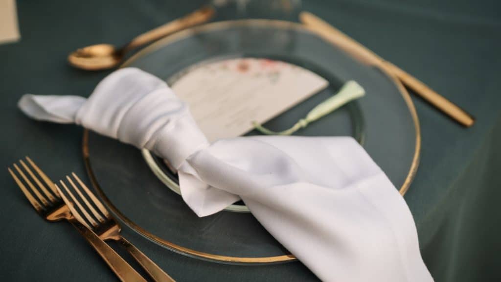 Elegant table setting for wedding, featuring gold cutlery, white napkin, and decorative plate, perfect for wedding reception planning by ChiaraB Events.