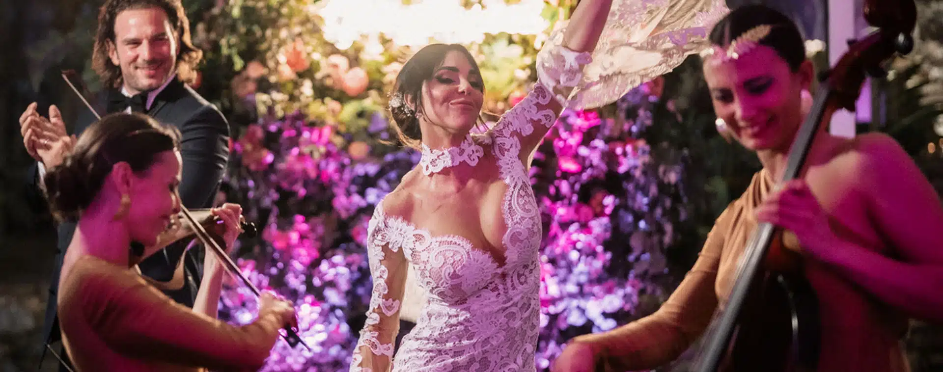 Donna in abito da sposa che danza con musicisti in un giardino illuminato di notte.