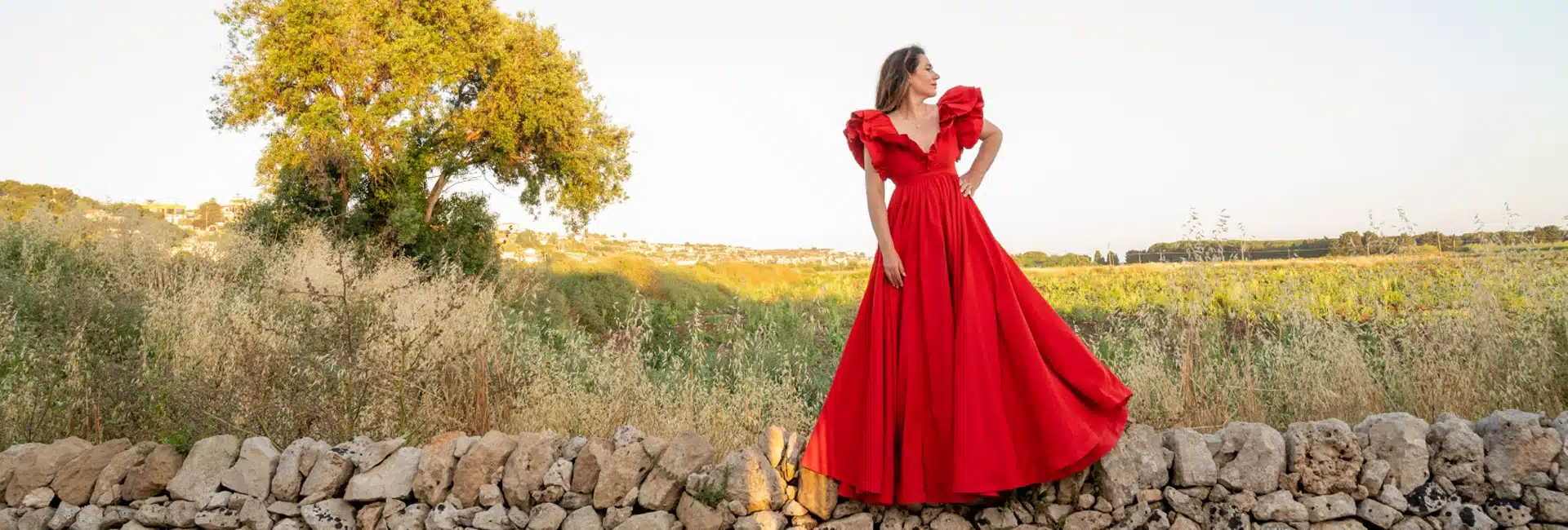 Elegante donna in abito da sposa rosso in un paesaggio rurale, servizi di wedding planning, atmosfera romantica, ChiaraB Events.