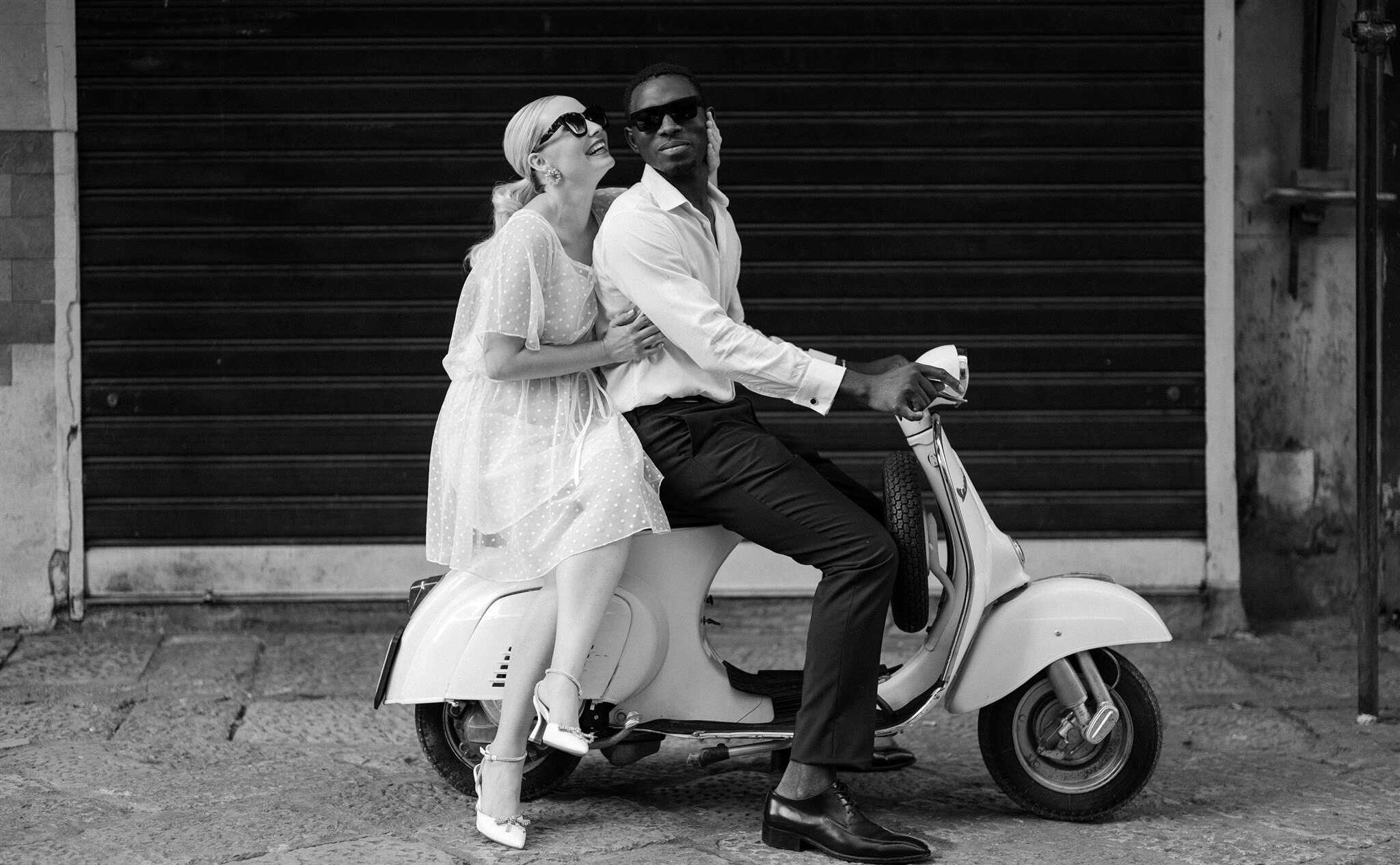 Coppia felice su scooter in strada, in un contesto urbano, durante un matrimonio, con un'atmosfera di gioia e libertà.