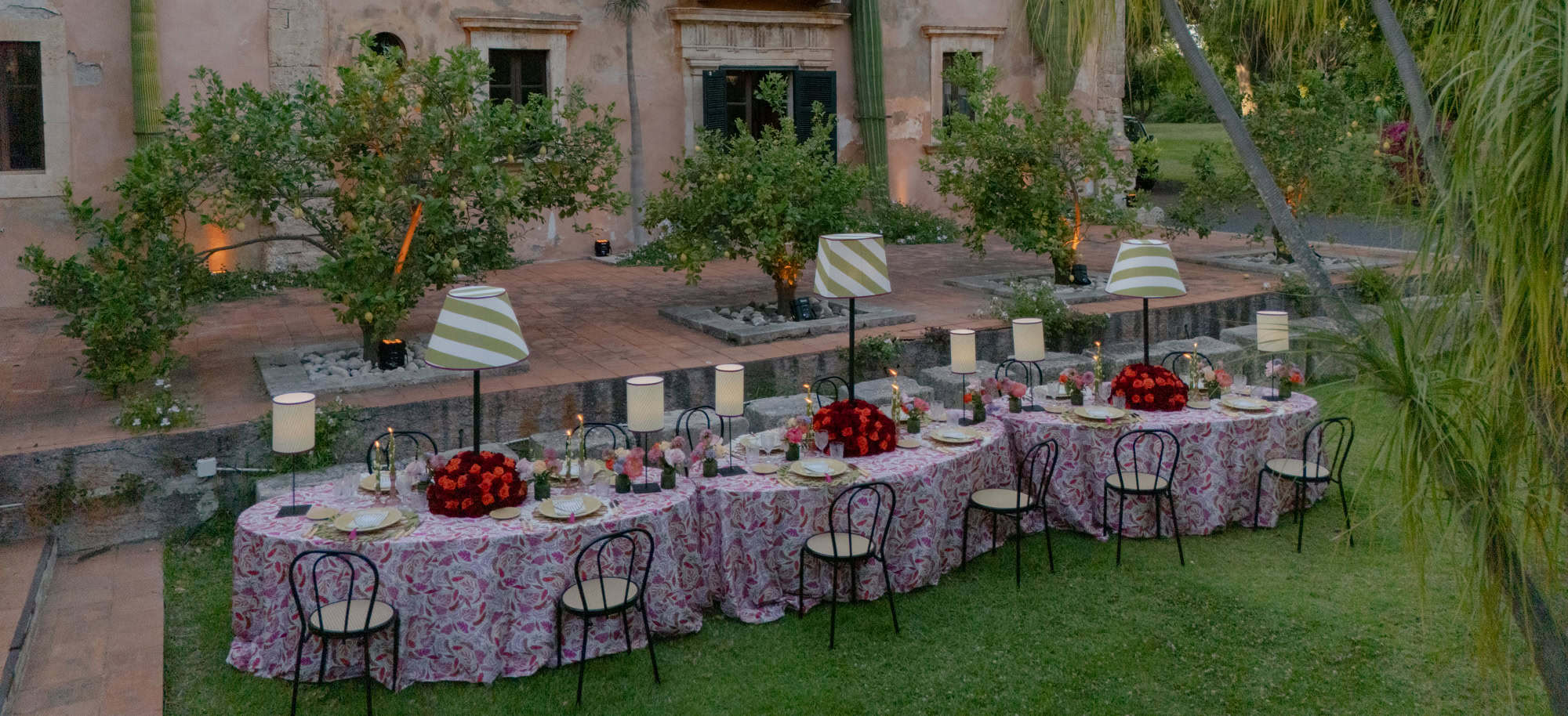 लाल फूलों, फूलों वाली मेज़पोश और मोमबत्तियों से सजी बाहरी शादी की मेज, एक रोमांटिक और सुरुचिपूर्ण शादी के लिए परफेक्ट।