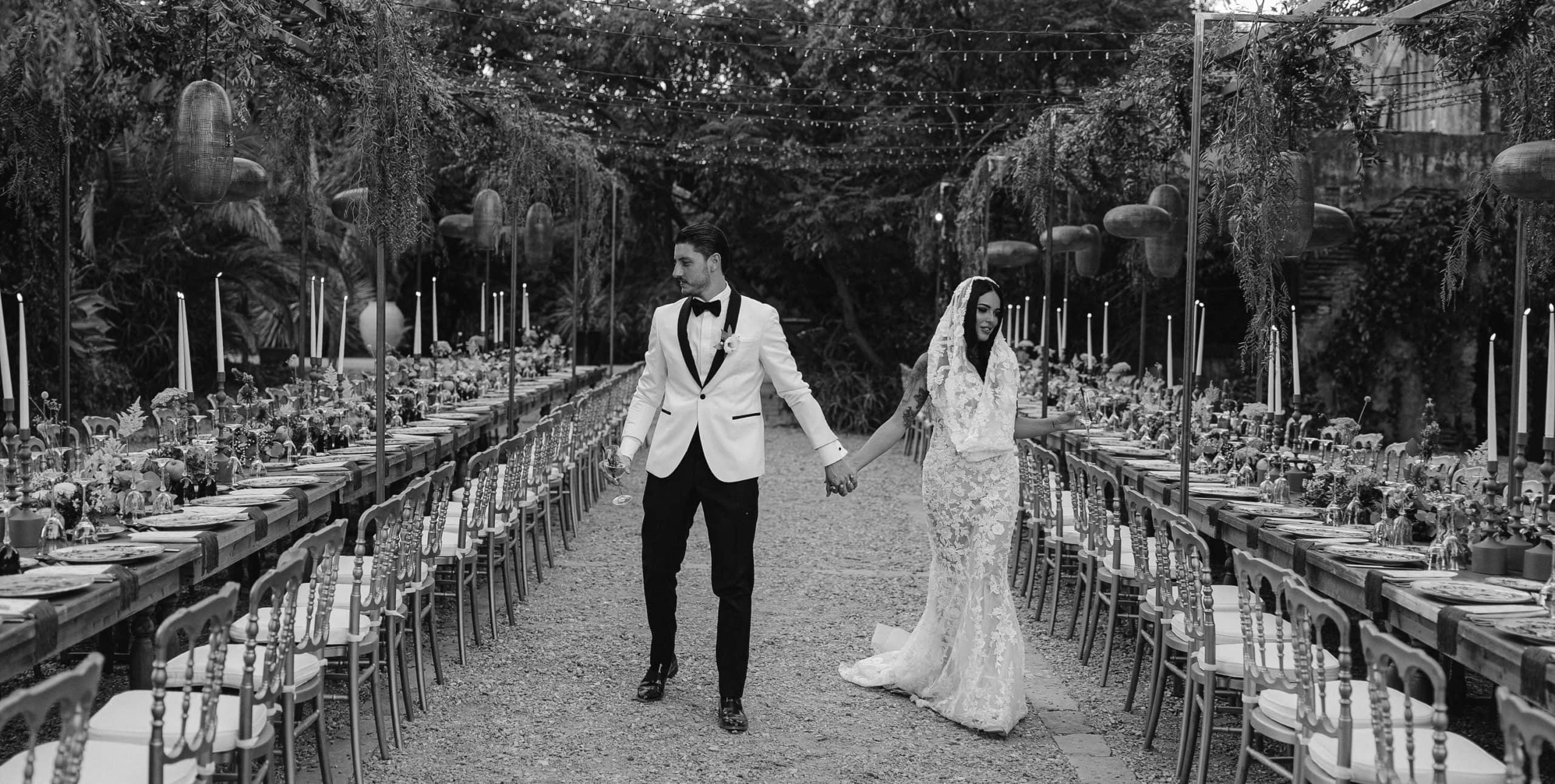 Coppia di sposi cammina mano nella mano in un matrimonio elegante, con tavoli decorati e atmosfera romantica, organizzato da ChiaraB Events Wedding Planner.