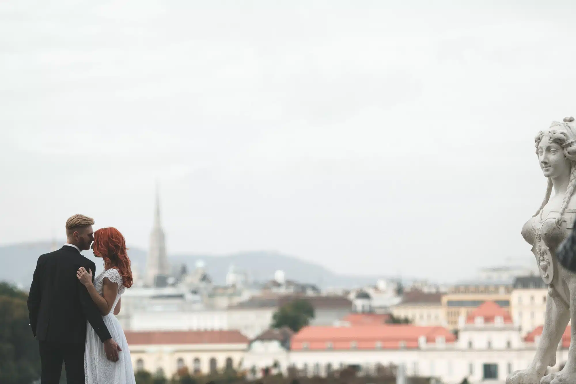Elegante coppia di sposi romantici su terrazza con vista sulla città, stile minimalista, abiti da matrimonio formali, servizio di wedding planning professionale.