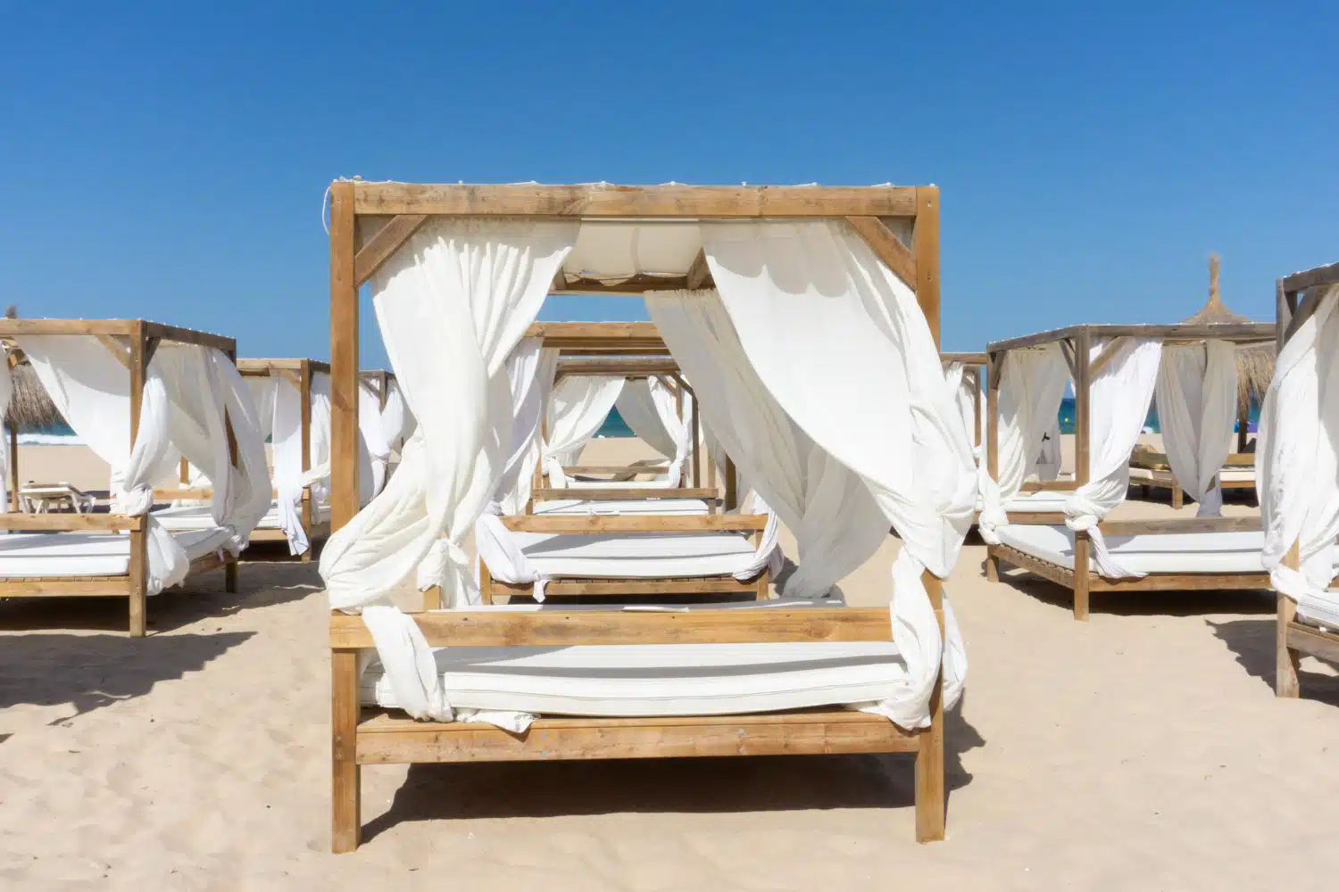 Cabanas de praia relaxantes com cortinas brancas e molduras de madeira num local de casamento à beira-mar.