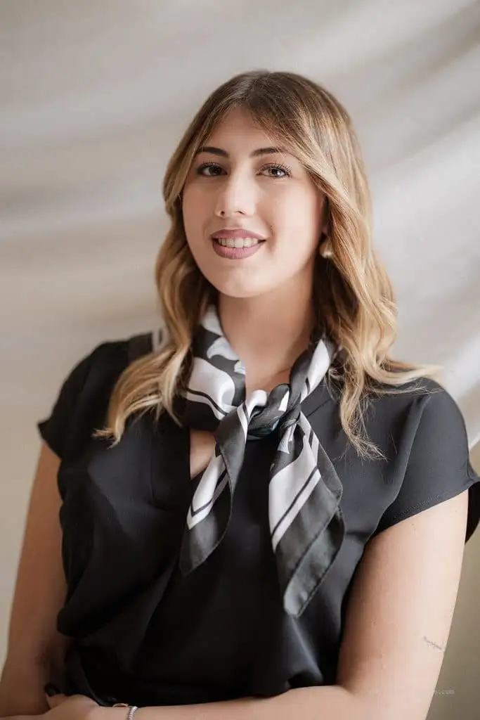 Beautiful smiling woman in black blazer and striped scarf, professionally involved in the wedding planner industry, representing elegance and style for weddings and special events.