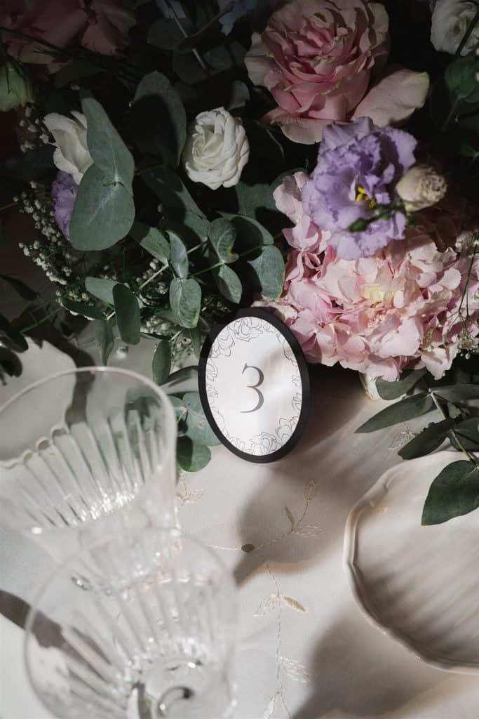 Elegante composizione floreale con numerazione tavolo, perfetta per matrimoni e eventi raffinati, decorata con fiori rosa, lilla e verde, creata da ChiaraB Events Wedding Planner.