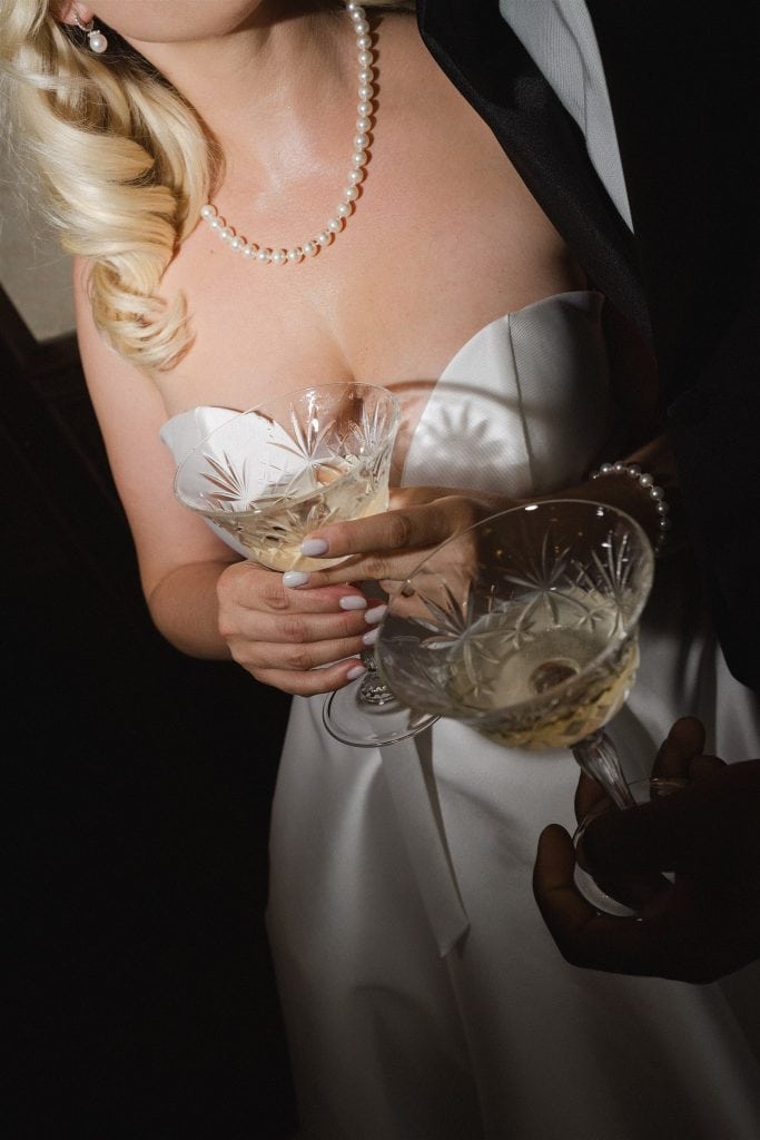 Un matrimonio elegante con la sposa in abito bianco e il partner che brinda con bicchieri di champagne, in un'atmosfera raffinata e celebrativa. Perfetto per servizi di wedding planning e organizzazio.