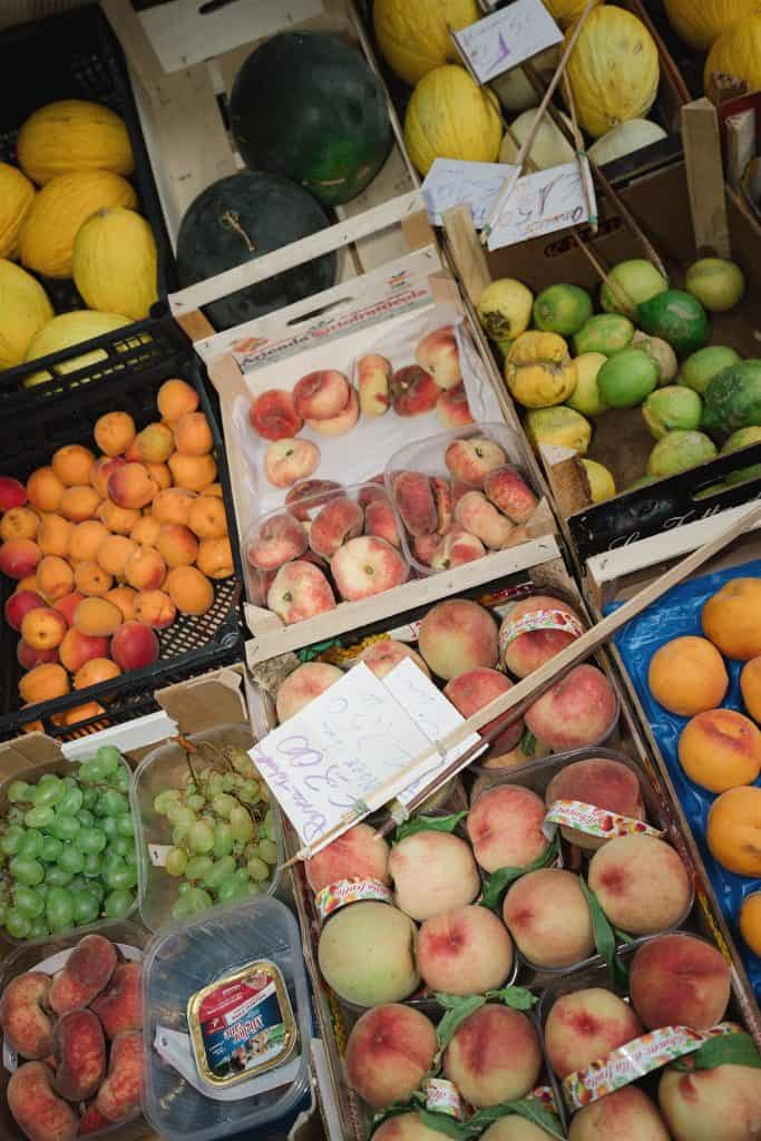 Pomodori, pesche e meloni freschi in bancarella di mercato, colorati e invitanti, pronti per essere acquistati.