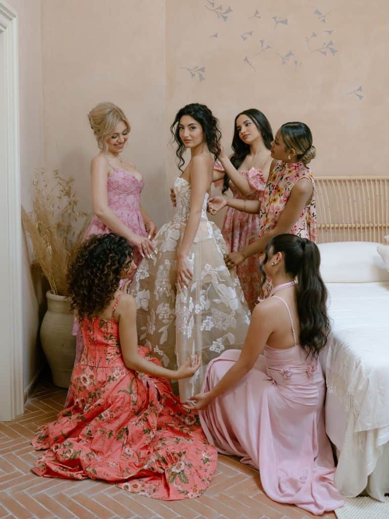 Elegant wedding dress with lace details, surrounded by friends helping to get ready for the wedding, in an intimate and refined setting, perfect for wedding planning and organizing services.