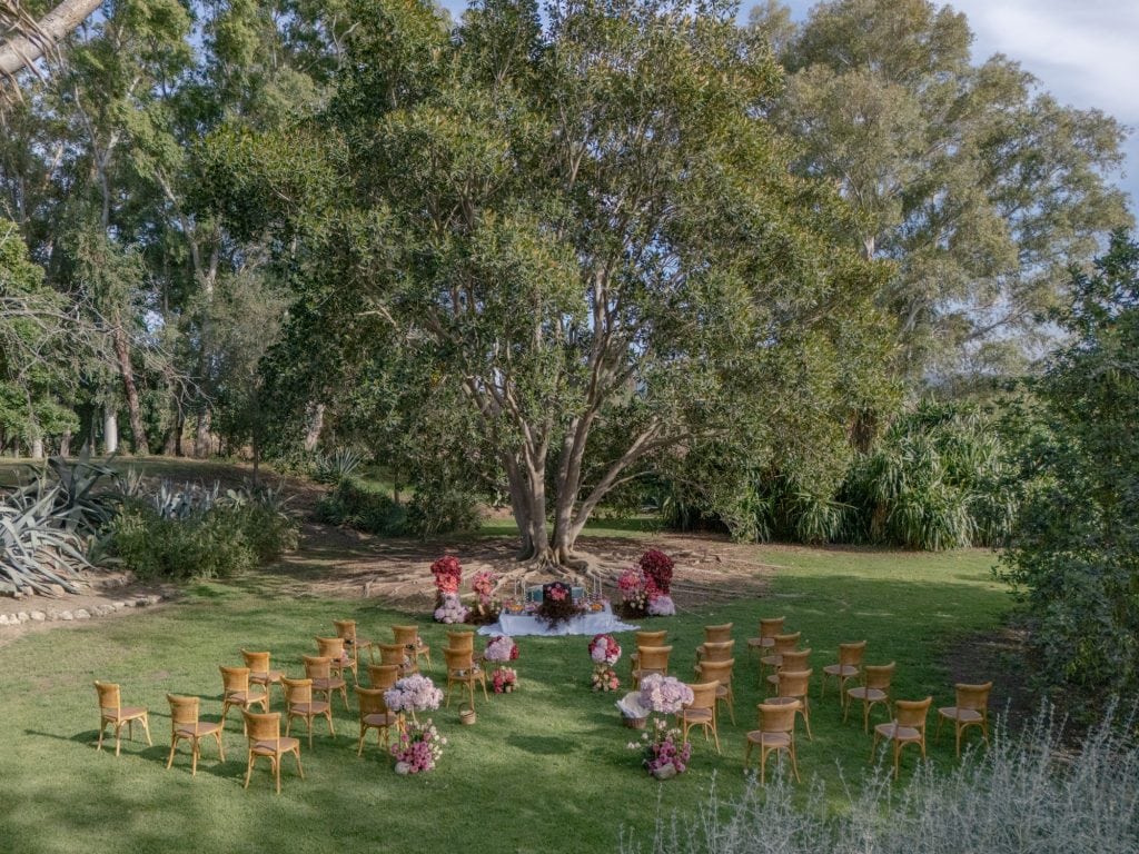 Outdoor seating in a green garden with wooden chairs and floral decorations for an outdoor wedding.