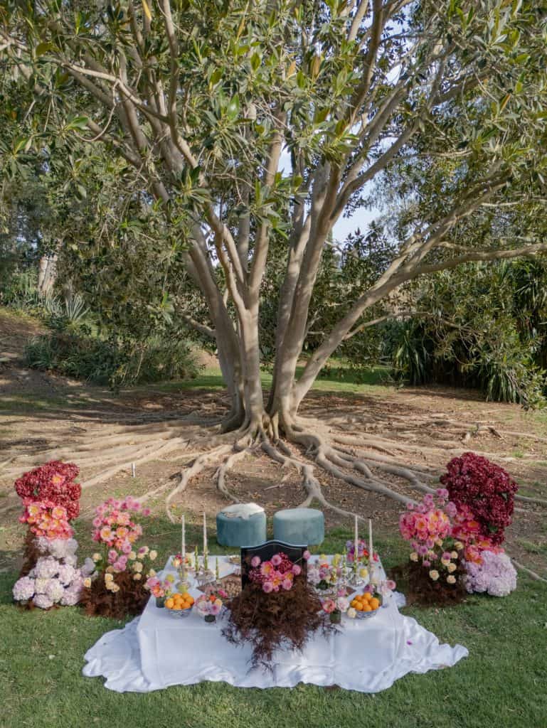 Panel of floral decorations and candles under a large tree, ideal for outdoor weddings, with colorful flowers and a romantic atmosphere, curated by ChiaraB Events Wedding Planner.