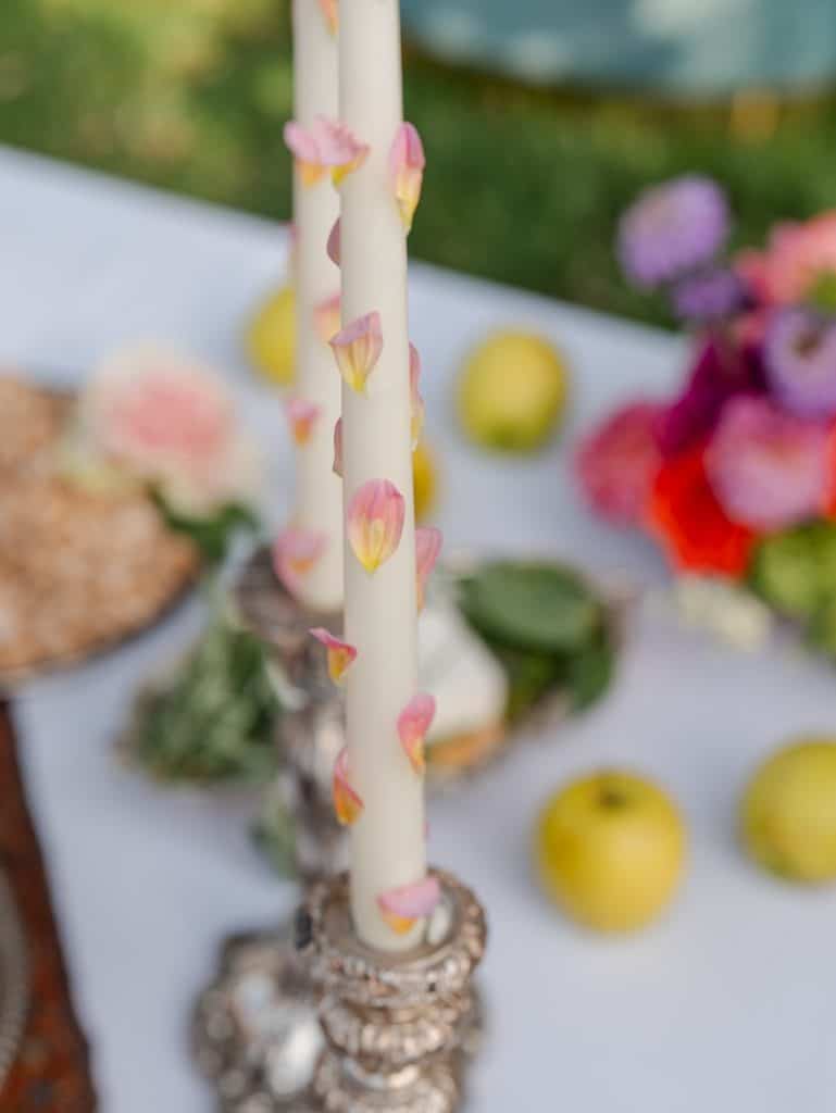 Flame decorated with pink flower petals, part of a floral arrangement for a wedding, with a background of colorful flowers and fresh fruit, ideal for romantic and refined events.