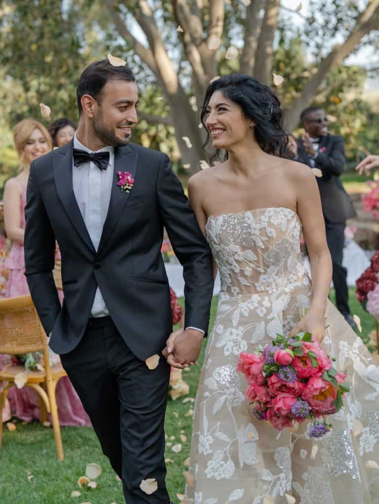 The romantic wedding with happy bride and groom holding hands outdoors, surrounded by friends and floral decorations, representing a special event organized by ChiaraB Events, wedding planner.
