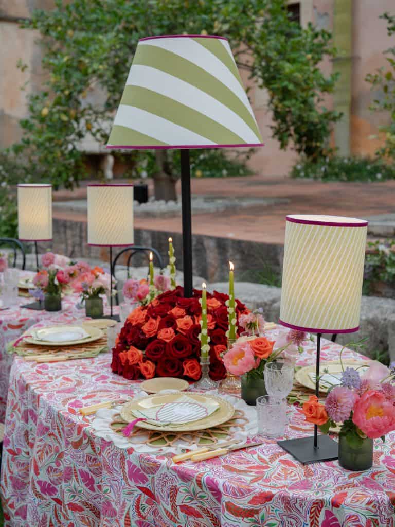 Outdoor dining table decorated with colorful flowers, candelabras, and table lamps, perfect for weddings and elegant events, with a romantic and refined atmosphere.