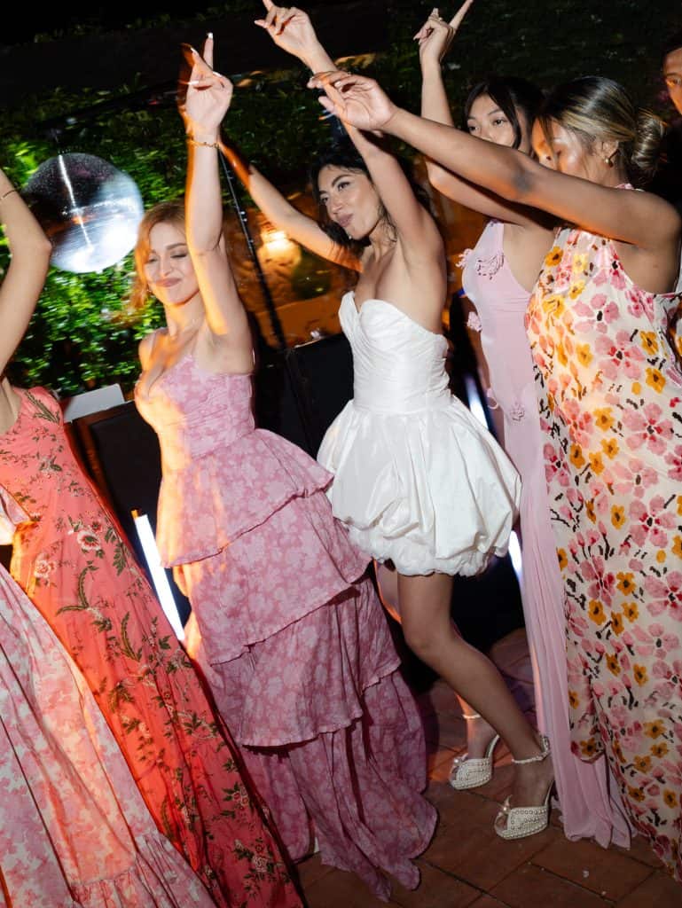 Elegant group of women dancing and having fun at an outdoor wedding, with soft lights and floral decorations, representing the event organization of ChiaraB Events Wedding Planner.
