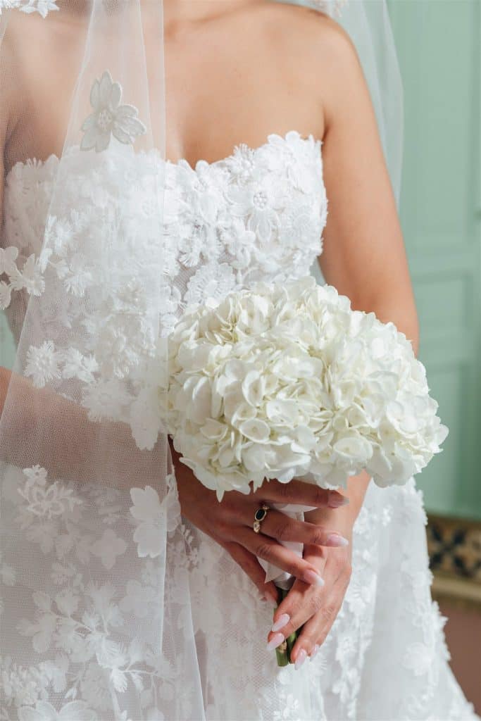 Un bouquet di fiori bianchi con una sposa in abito da matrimonio con dettagli in pizzo e velo, pronta per il suo giorno speciale.