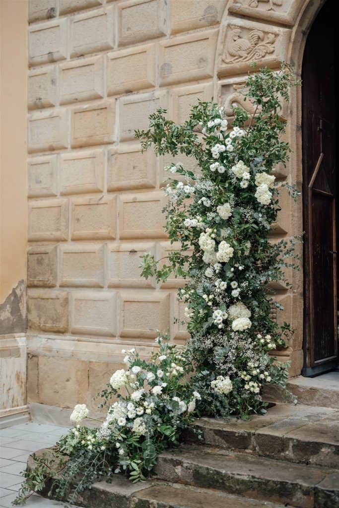 Tappeto floreale bianco e verde decorativo all'ingresso di un edificio storico, ideale per matrimoni e eventi eleganti, con dettagli raffinati e atmosfera romantica.