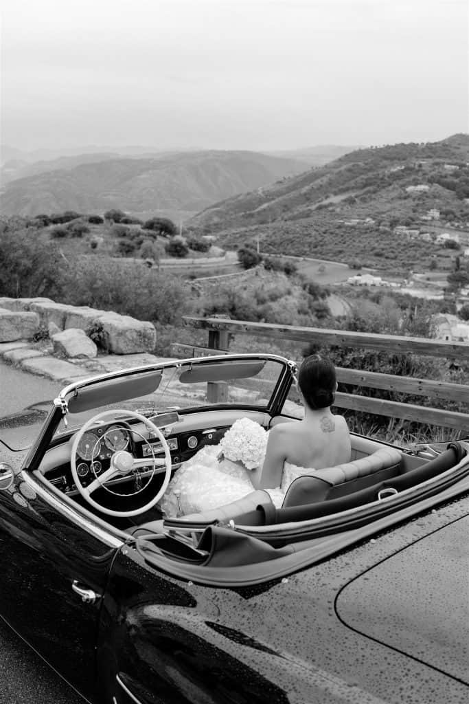 Auto d'epoca con sposa seduta, vista panoramica sulle colline toscane, perfetto per servizi fotografici di matrimoni romantici e wedding planning di lusso, ChiaraB Events.