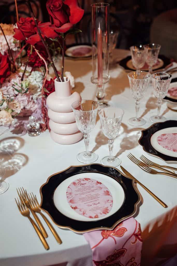 Vaso decorativo con fiori rossi e tavola elegante per matrimonio, allestimento raffinato con cristalli e posate dorate, perfetto per eventi nuziali di lusso e wedding planning professionale.