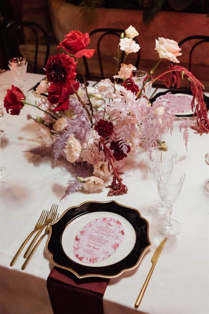 Elegante centrotavola floreale con rose rosse, bianche e fucsia, decorato con foglie e fiori di vari colori, ideale per matrimoni e eventi raffinati, allestimento di alta classe.
