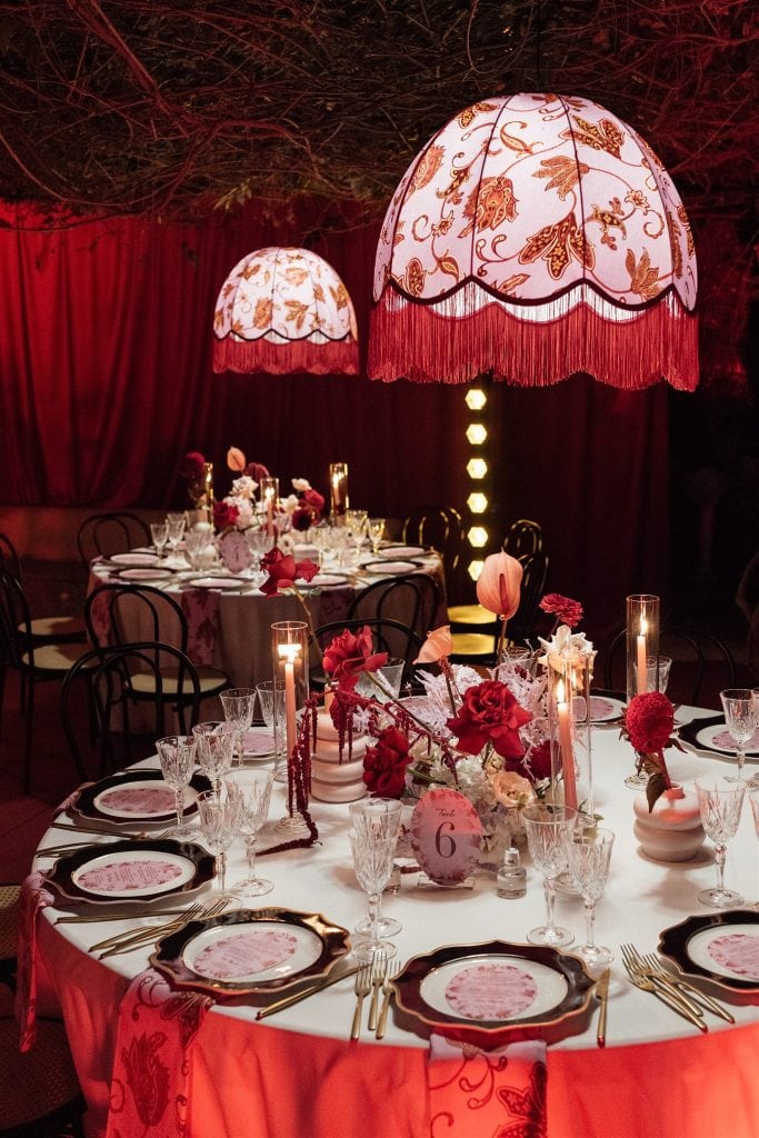 Elegante allestimento per matrimonio con tavolo rotondo decorato con fiori rosa e rosso, illuminazione soffusa e lampade decorative, perfetto per wedding planner e eventi romantici.