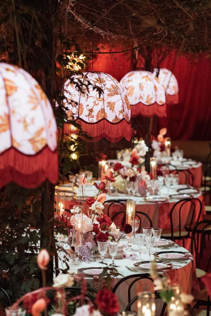 Lampade da tavolo decorative con paralumi floreali, illuminano elegantemente una sala da pranzo all'aperto per un matrimonio o evento speciale, creando un'atmosfera romantica e raffinata.