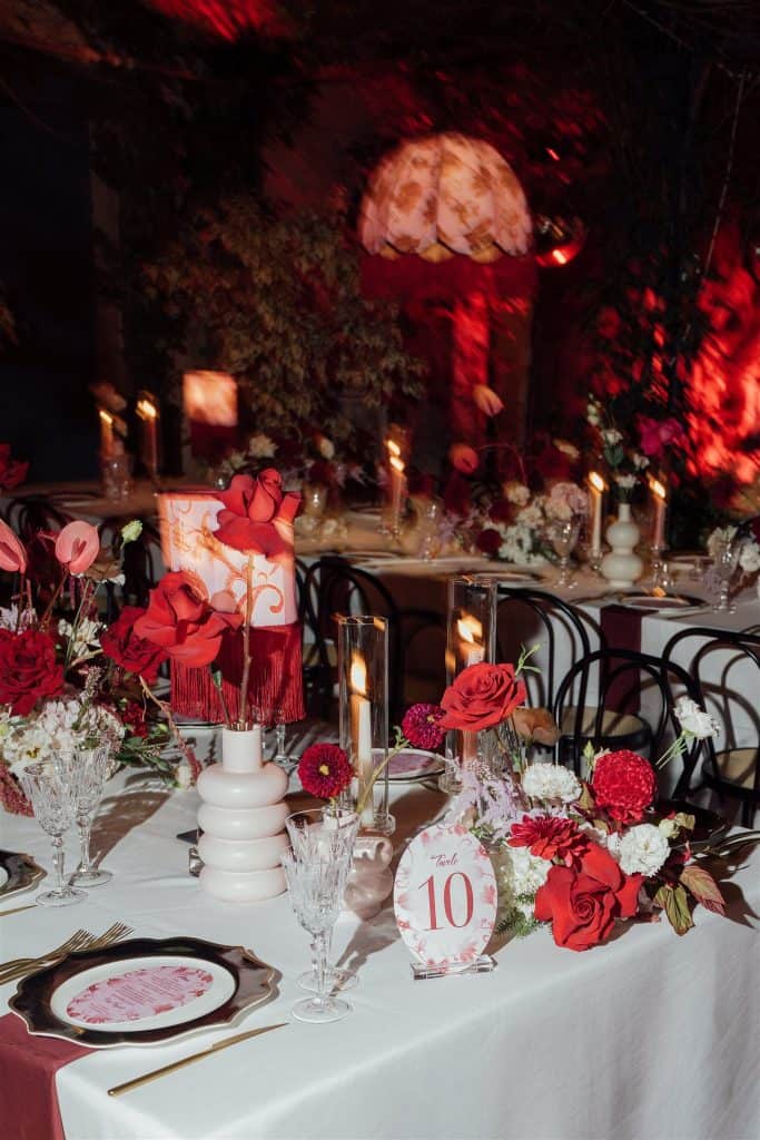 Tavola decorata per matrimonio con fiori rossi e candele, atmosfera romantica e elegante, perfetta per eventi nuziali raffinati e personalizzati, con dettagli di design e atmosfera intima.