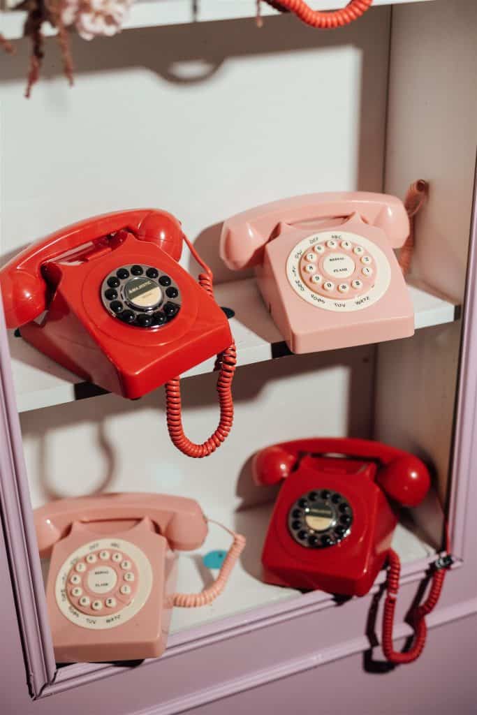 Telefono vintage rosso e rosa, decorativo, in stile retrò, su scaffale bianco, con sfondo neutro, elemento di design per eventi e matrimoni, perfetto per decorazioni eleganti e originali.