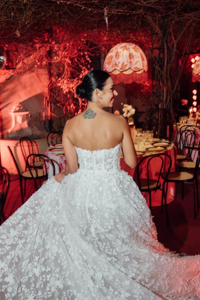 Elegante sposa in abito da matrimonio bianco con dettagli floreali, in un ambiente romantico e intimo con luci calde e decorazioni floreali, perfetto per servizi di wedding planning e organizzazione m.