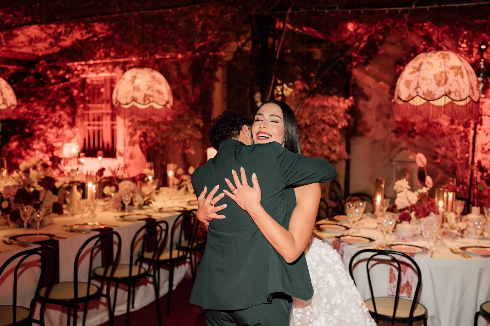 Sposi felici che si abbracciano durante il ricevimento di nozze in un elegante venue decorato con luci calde e fiori, perfetto per wedding planning e eventi speciali.