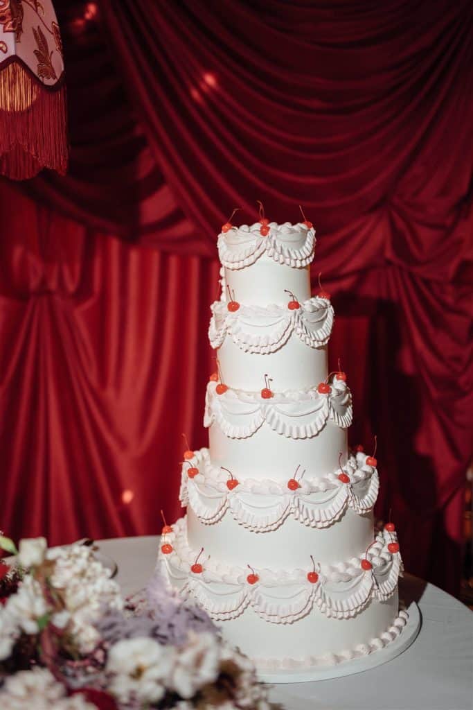 Un dolce matrimonio con torta nuziale a cinque piani decorata con dettagli eleganti e fiocchi rossi, perfetta per un matrimonio romantico e sofisticato. Ideale per servizi di wedding planning e allest.