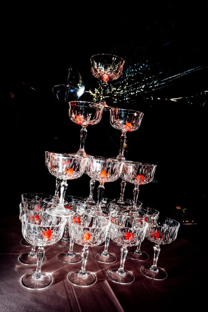 Luci e riflessi su un'installazione di calici di champagne in vetro, con un effetto di esplosione di champagne e scintille sullo sfondo, perfetta per eventi e matrimoni eleganti.