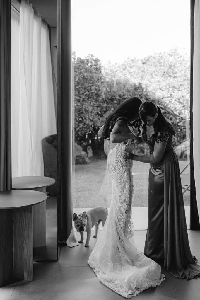 Momento emozionante tra la sposa e la damigella prima del matrimonio, con cane al seguito, in un ambiente luminoso e elegante, perfetto per servizi di wedding planning e organizzazione eventi.