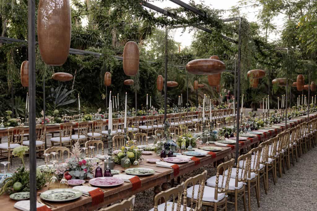 Allestimento elegante per matrimonio con tavolo lungo, decorazioni floreali, candele e sedie dorate in un giardino naturale, perfetto per eventi nuziali raffinati e personalizzati.