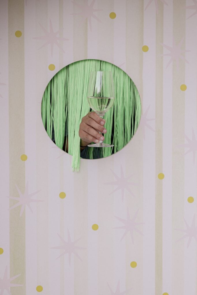 Un bicchiere di champagne tenuto da una mano, inserito in un cerchio verde con sfondo decorativo di stelle e linee, ideale per eventi e feste eleganti.