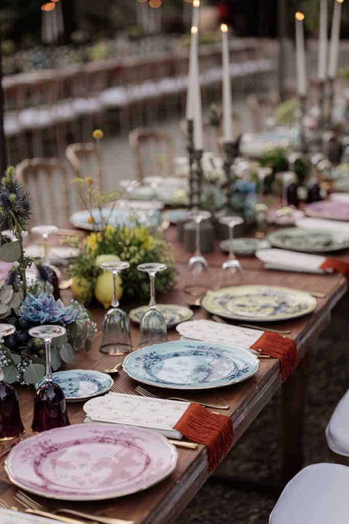 Elegante tavola per matrimonio con piatti decorativi, bicchieri colorati e candele, perfetta per un evento nuziale raffinato e romantico.