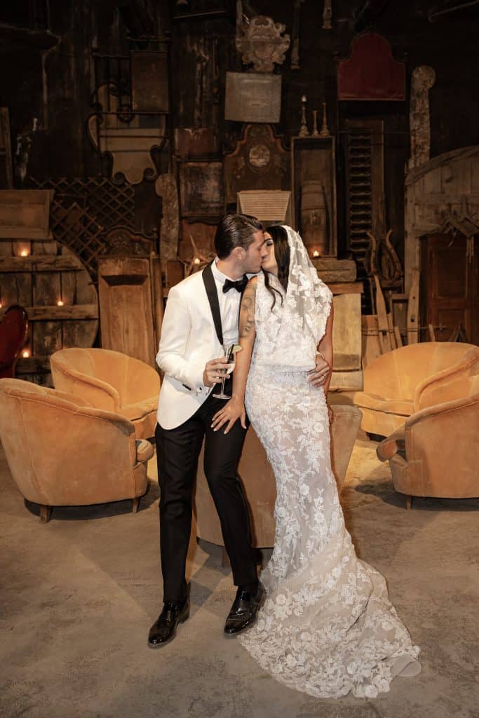Un matrimonio elegante con sposi in abiti da sera e abito da sposa in pizzo, in un ambiente vintage con arredi in legno e luci calde, perfetto per un matrimonio romantico e sofisticato.