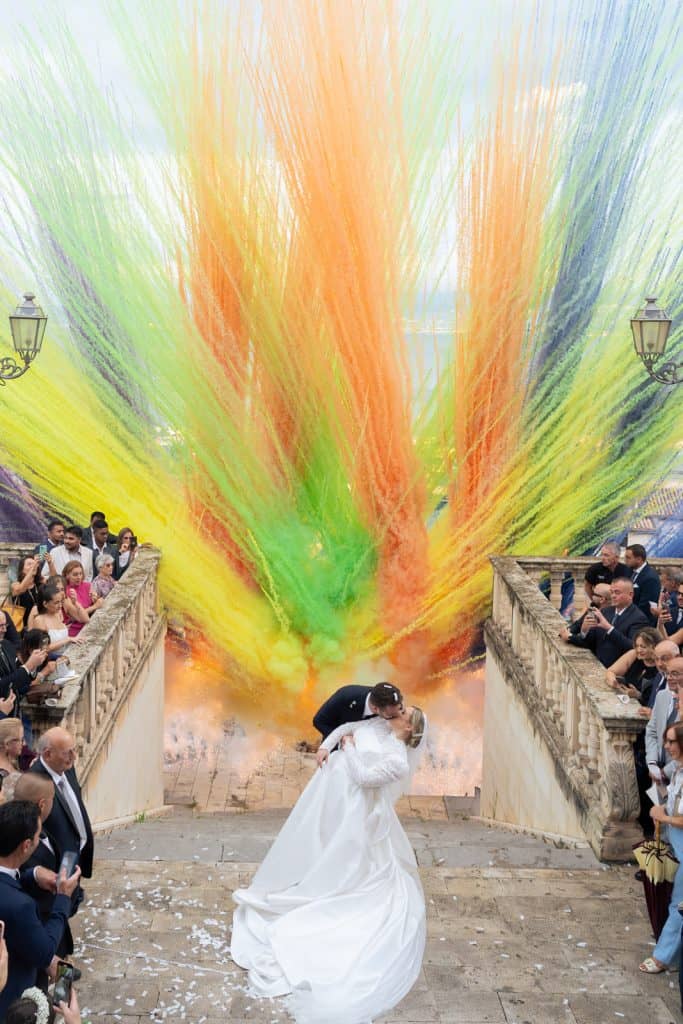 Un matrimonio con esplosione di colori, con sposi che si baciano sotto un lancio di polvere colorata durante il matrimonio, evento organizzato da ChiaraB Events Wedding Planner, in un ambiente elegant.