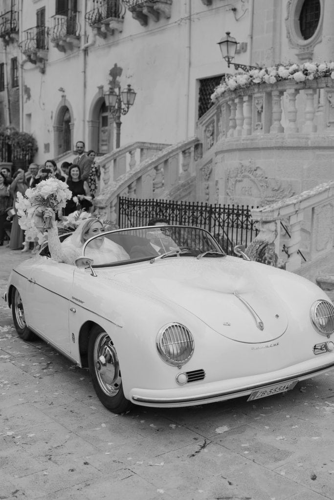 Un'auto d'epoca bianca, cabriolet, parcheggiata davanti a un edificio storico con decorazioni floreali, durante un matrimonio elegante organizzato da ChiaraB Events Wedding Planner.