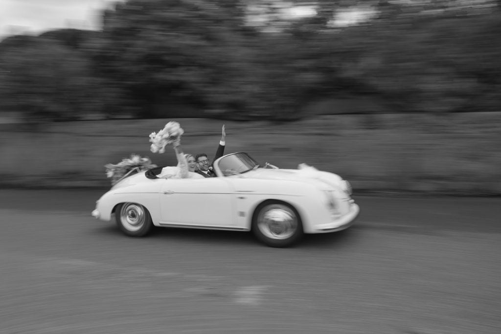 Un'auto d'epoca bianca in movimento su strada, decorata con fiori e nastri per un matrimonio elegante e romantico, perfetta per servizi di wedding planning e eventi speciali.