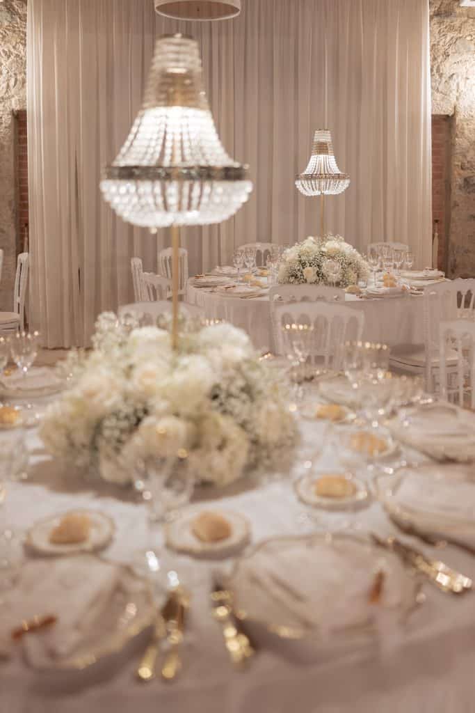 Elegante allestimento per matrimonio con tavoli decorati con fiori bianchi, candelabri e dettagli raffinati, perfetto per un wedding planner di alta classe.
