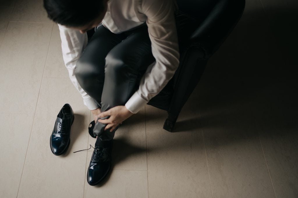L'uomo si sta allacciando le scarpe eleganti, seduto su una poltrona in un ambiente moderno e minimalista.